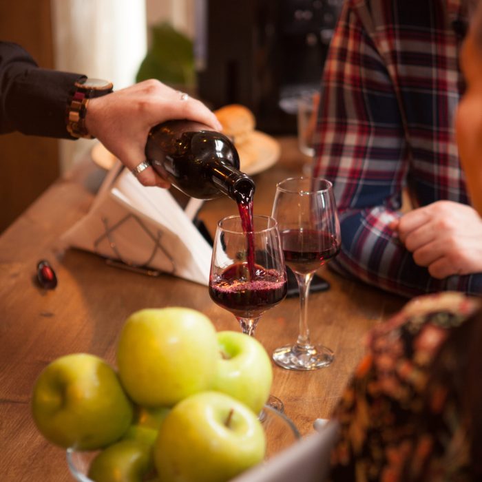 Bartender pouring red wine from a bottle in a wine glass. Hipster pub.